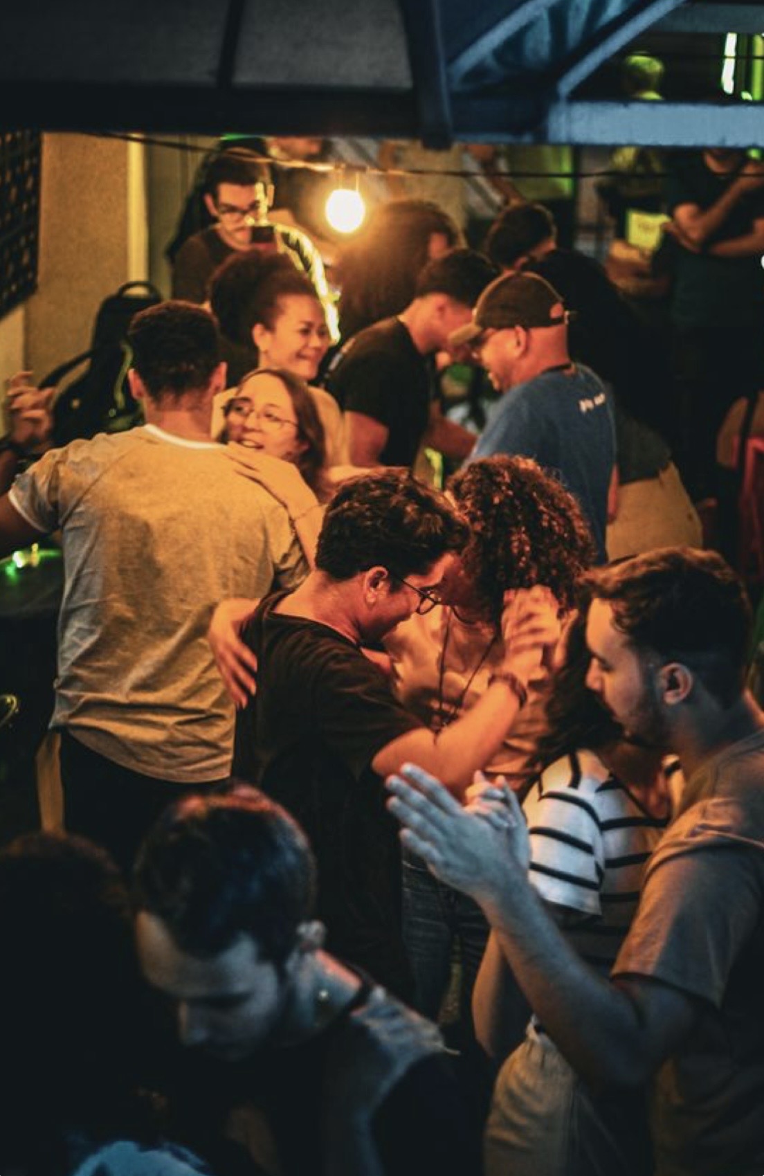 Bachata social dancers in close embrace under string lights