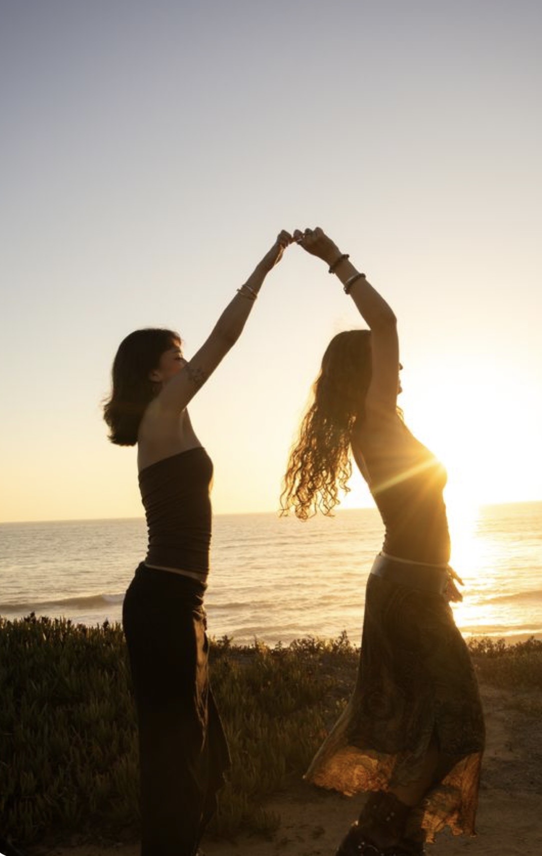 Two friends dancing at sunset by the ocean